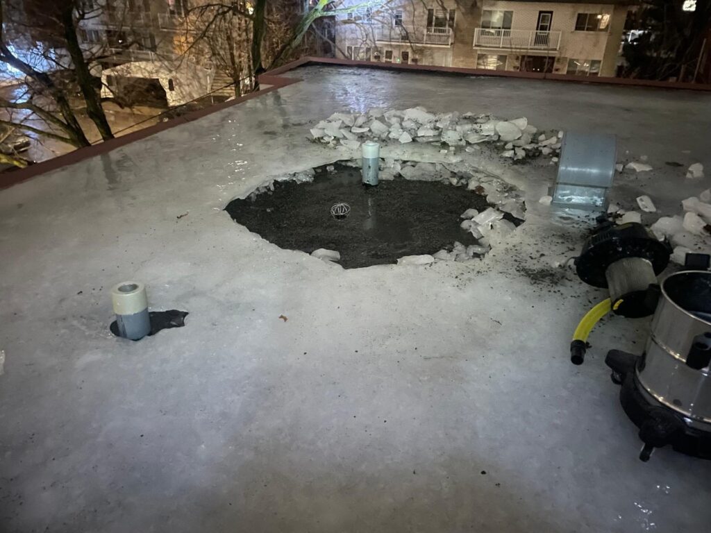 En hiver, la glace s'est formée par-dessus l'eau accumulée : on la casse autour du drain et on aspire l'eau.