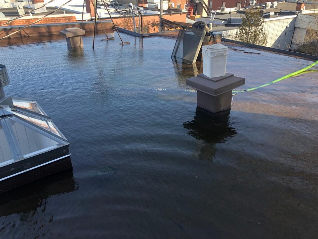 Accumulation d'eau sur un toit plat : l'eau monte jusqu'au lanterneau et à la base des évents.